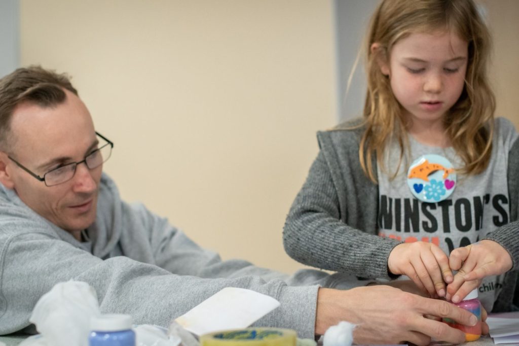 Winston's Wish practitioner helping a young girl to make a memory jar, a jar filled with coloured salts representing memories
