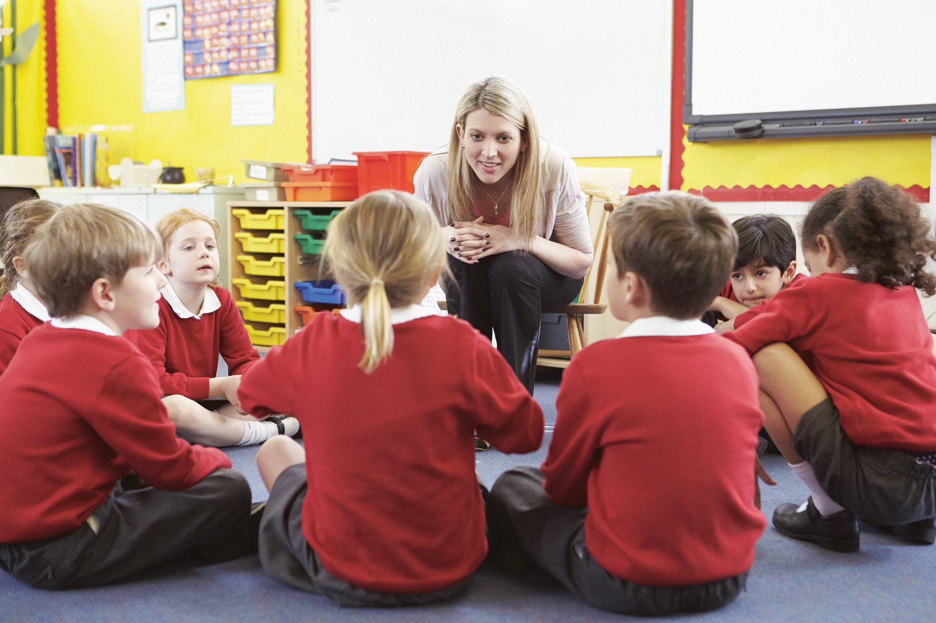 School classroom, female teacher crouching down surrounded by young children in school uniform