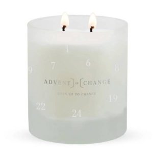white candle with two wicks, both are lit in cylindrical transparent frosted glass holder, the words "advewnt for change" are printed on the front of the candle
