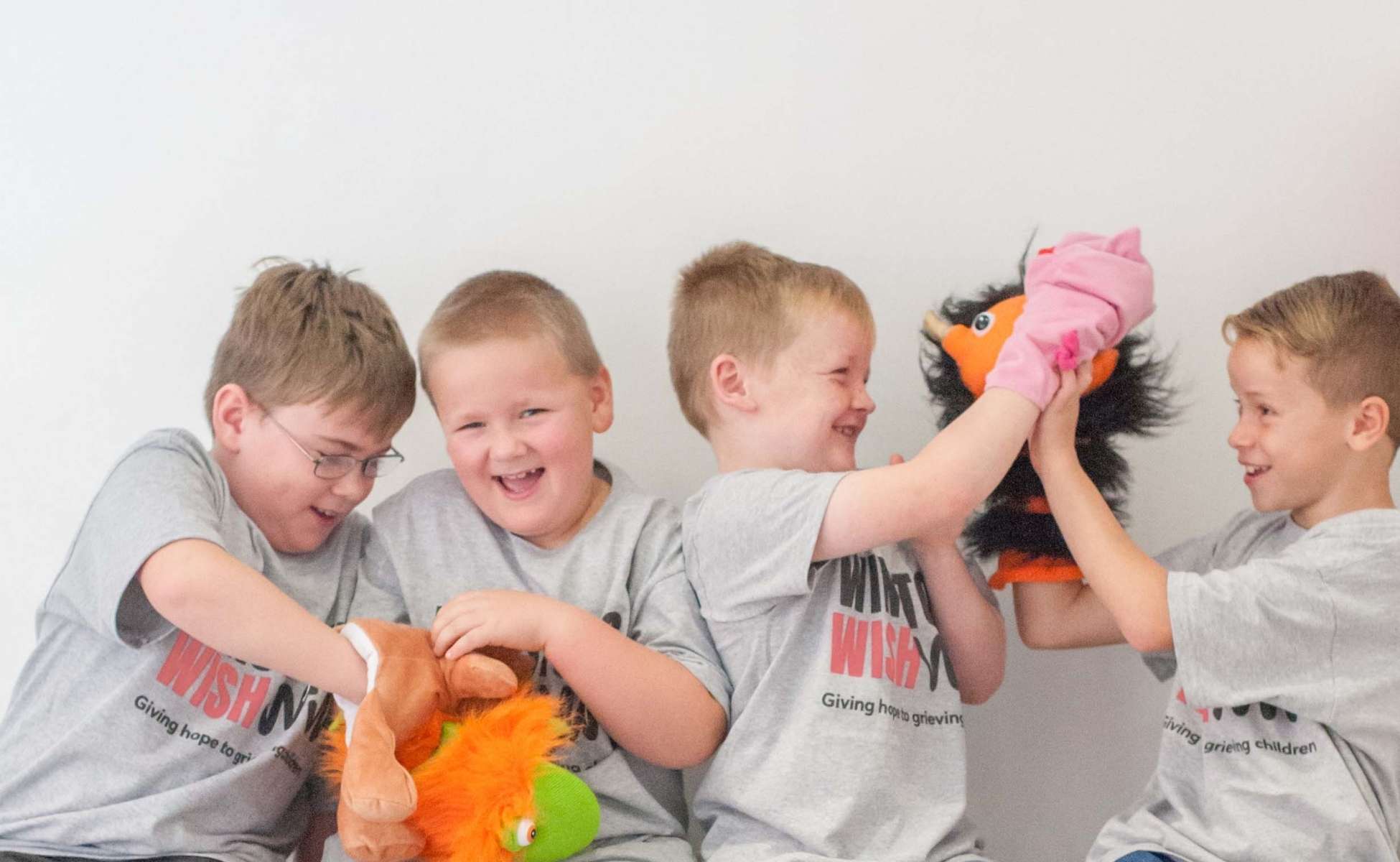 Four young boys in Winston's Wish t-shirts playing with puppets