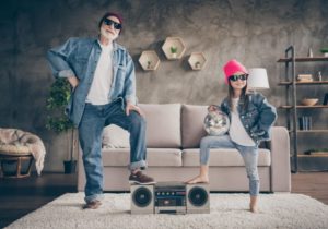 man and girl standing in front of sofa with feet on a stereo, they are wearing sunglasses and denim