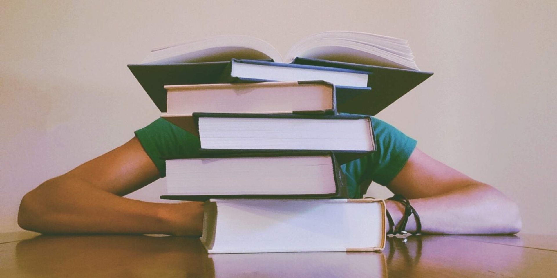 University student with head on hands behind a pile of books