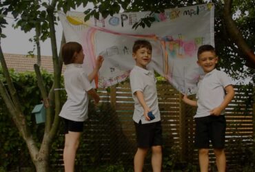 Three children in school uniform hanging a sign in a garden - Growing Hope - Winston's Wish