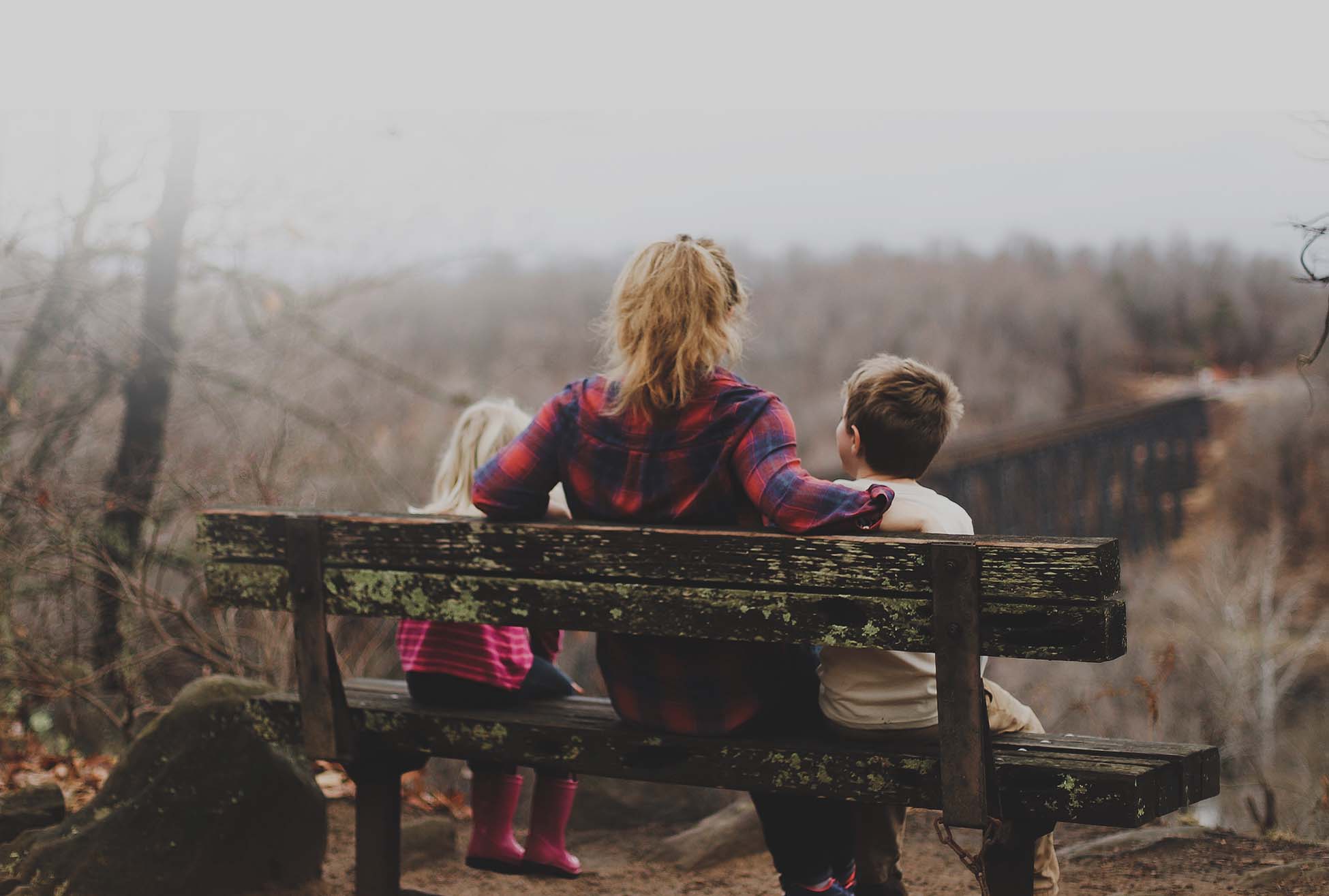 Mum and two young children sat on a bench looking at countryside - bereavement support services from Winston's Wish