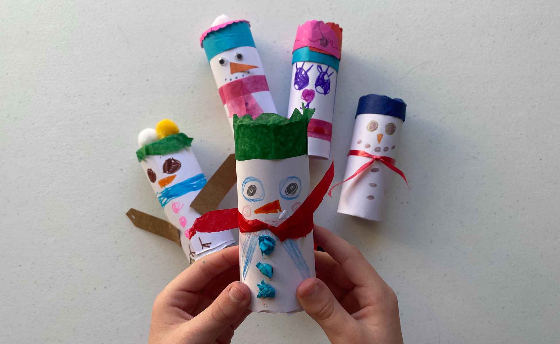 Child's hands holding a snowman made from a toilet roll tube. Step two of snowman strike Christmas activity