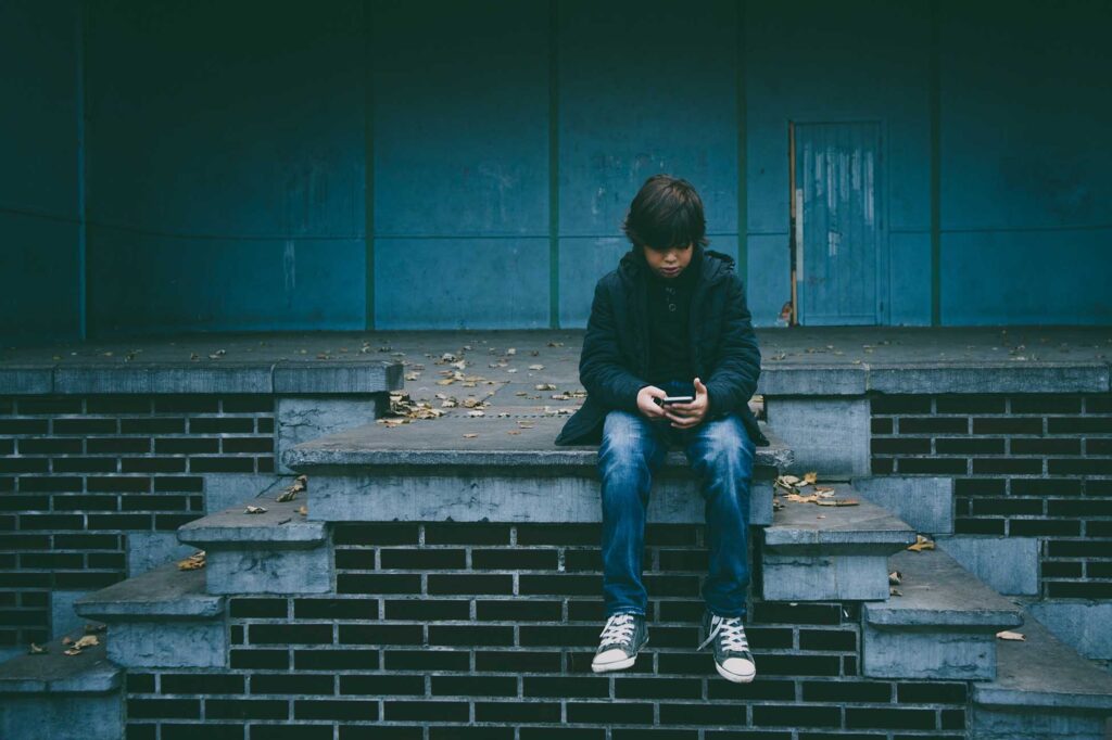 Teenager sat on a wall, texting on a phone - Winston's Wish Crisis Messenger