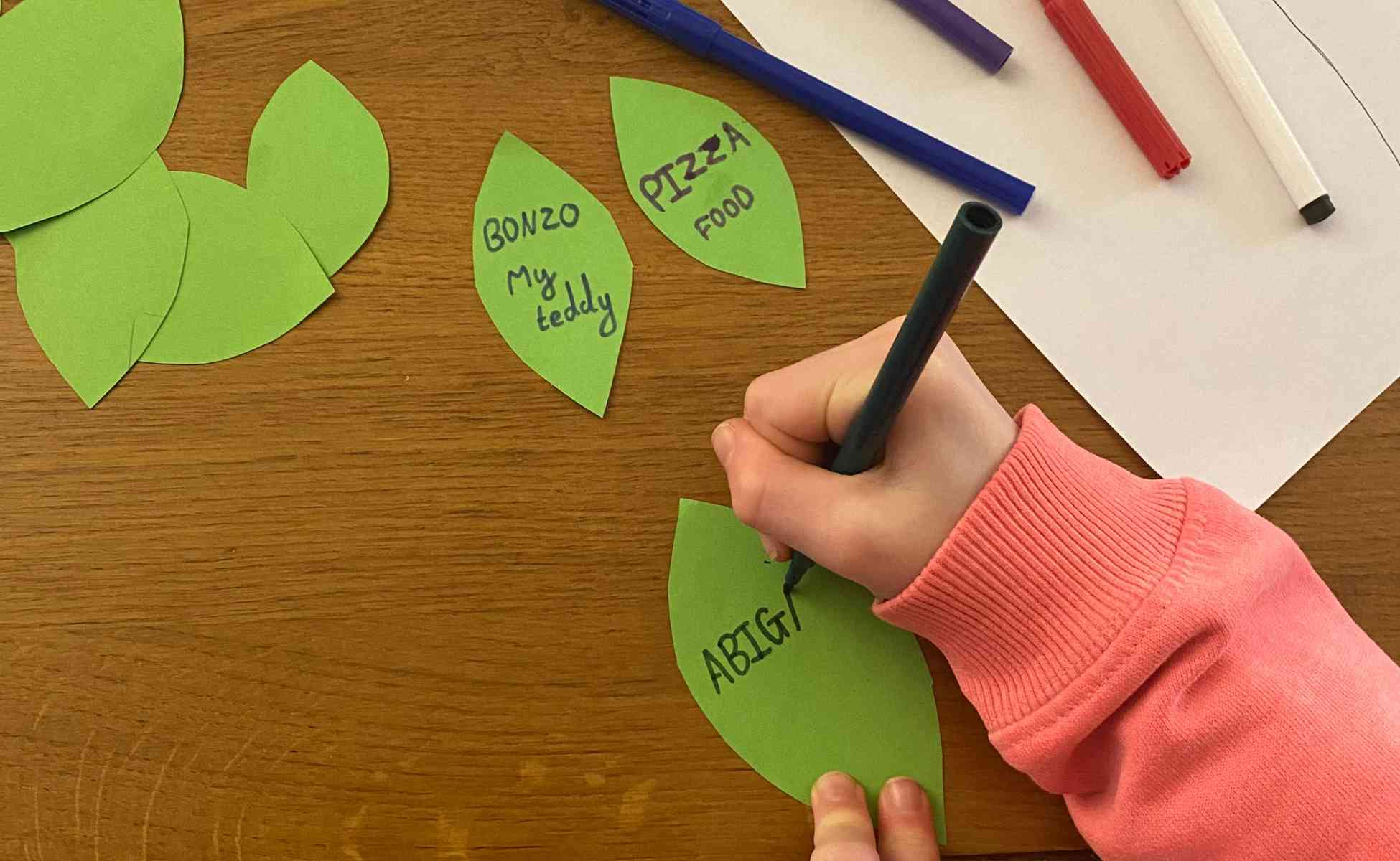 Photo of child's hand writing on a leaf shape - Thankful tree activity, step 5