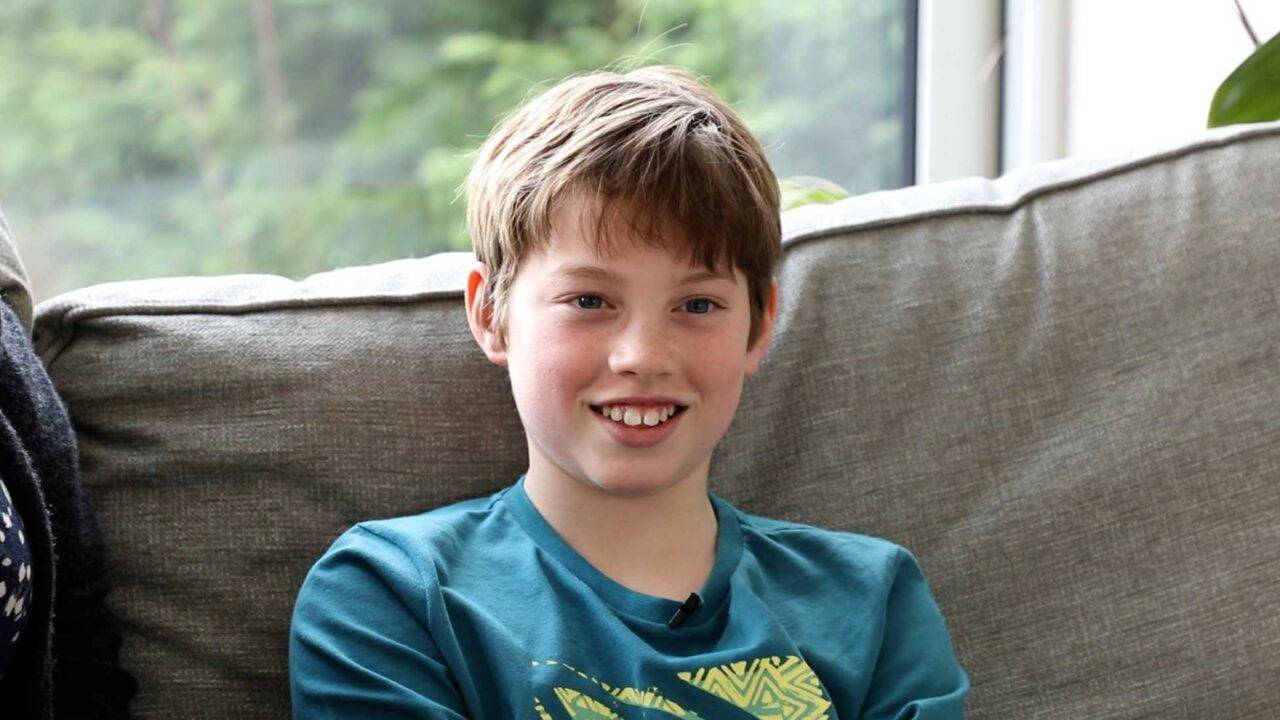 Photo of 11-year-old Harvey sat on a sofa, smiling at the camera