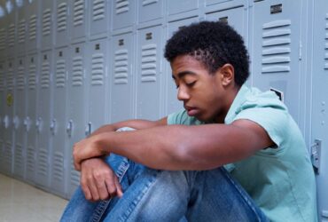 Teenage boy sat against school lockers looking sad