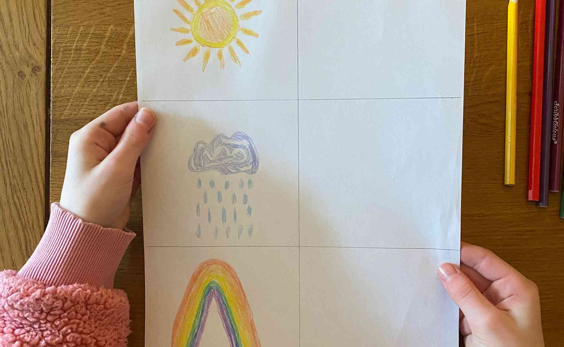 Photo of a child's hands holding a piece of paper with a grief of six boxes and drawings of a sun, rain cloud and rainbow in the three left boxes - Winston's wish Rainbow Review activity, step 2