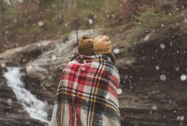 Two young people wrapped in a blanket with snow falling