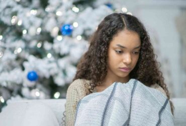Teenage girl looking sad with Christmas tree behind her