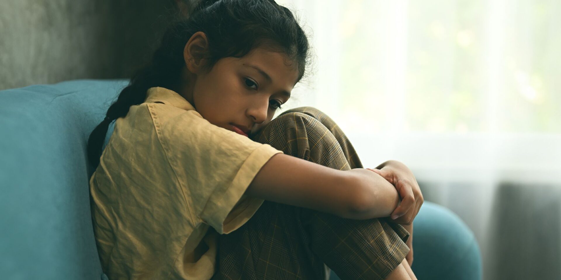 Young girl sat on the sofa, hugging her knees